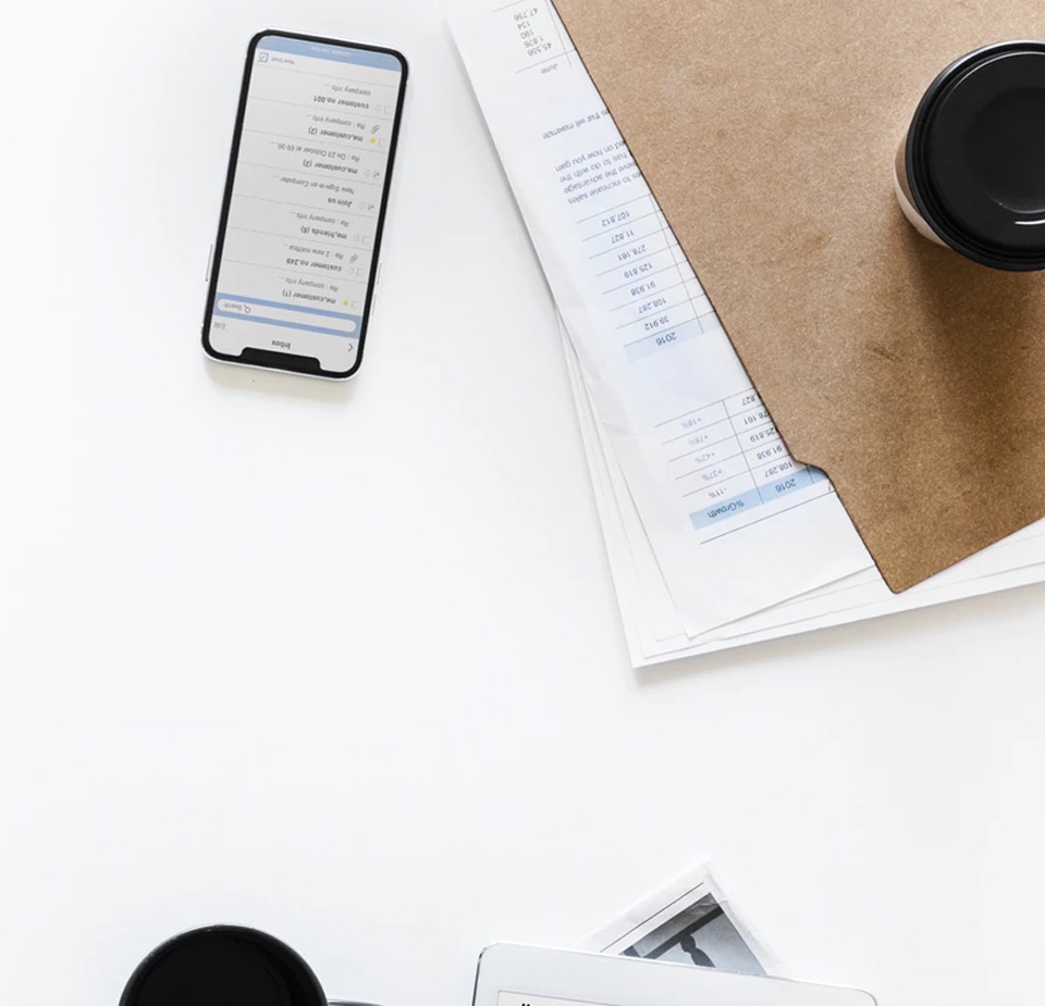 Bird's eye view of a desk with a phone, a file folder and a take-out coffee cup.